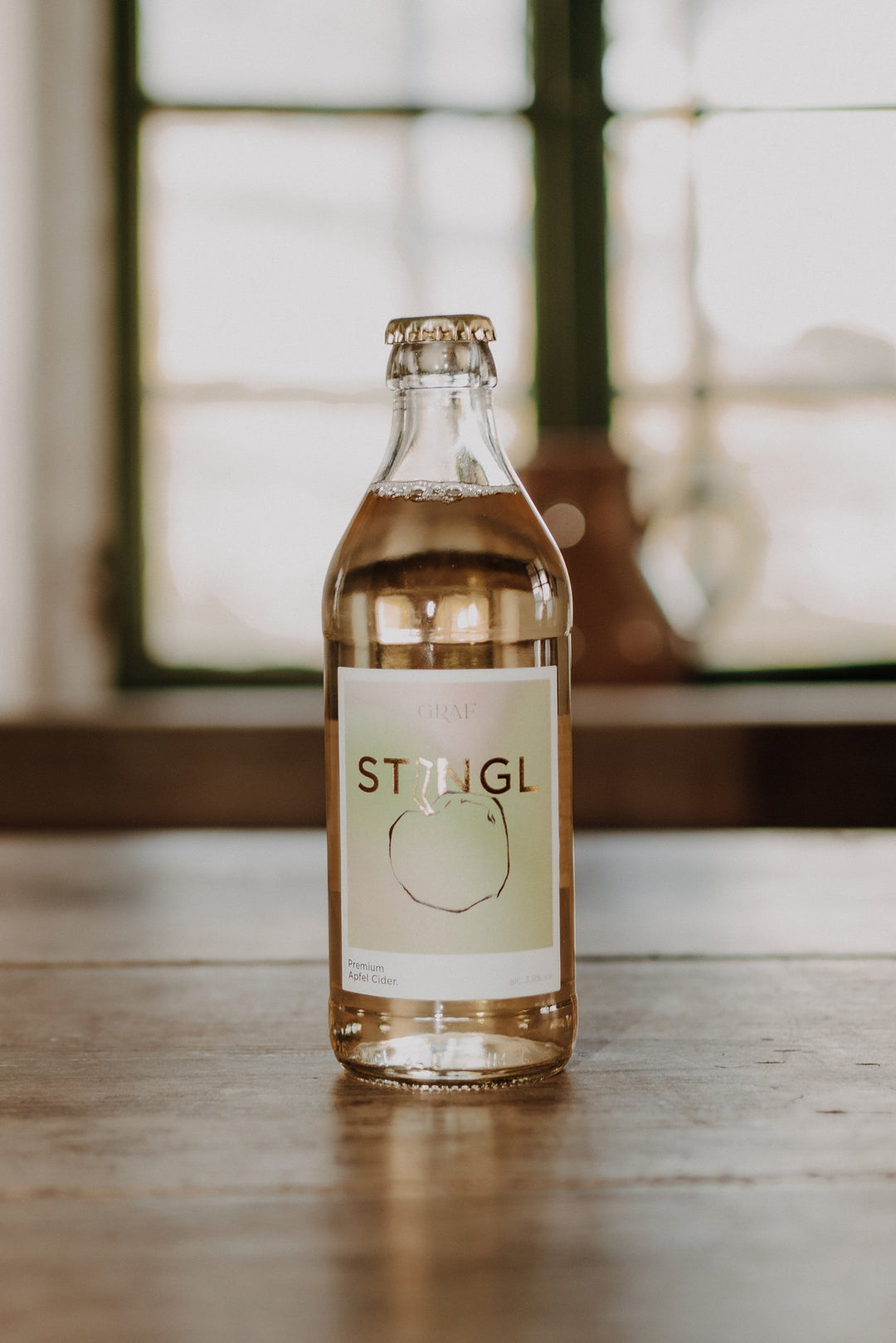 Stingl Premium Apfel Cider steht auf einer alten Tischplatte mit verschwommenen Hintergrund.